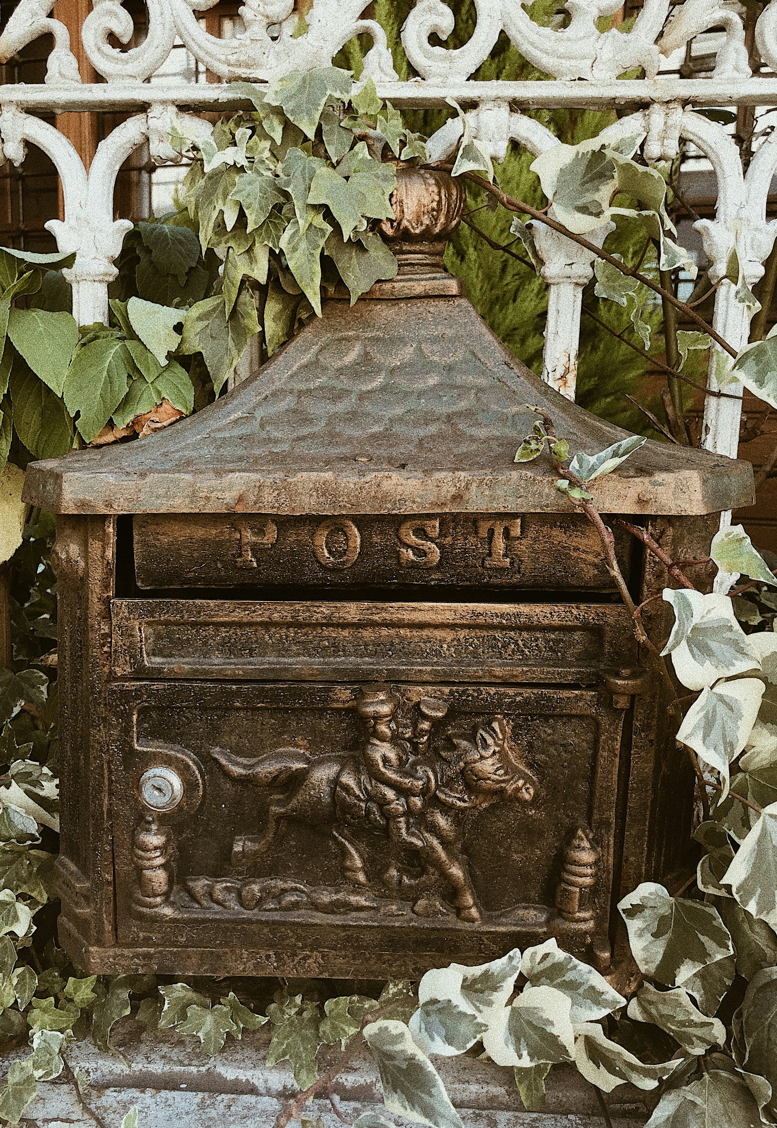 Antique cast iron POST mailbox embossed with a horse and rider, framed by ivy